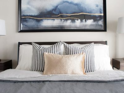 A piece of wall art featuring blue and gold added visual interest and height over the headboard in one of the condo bedroom designs